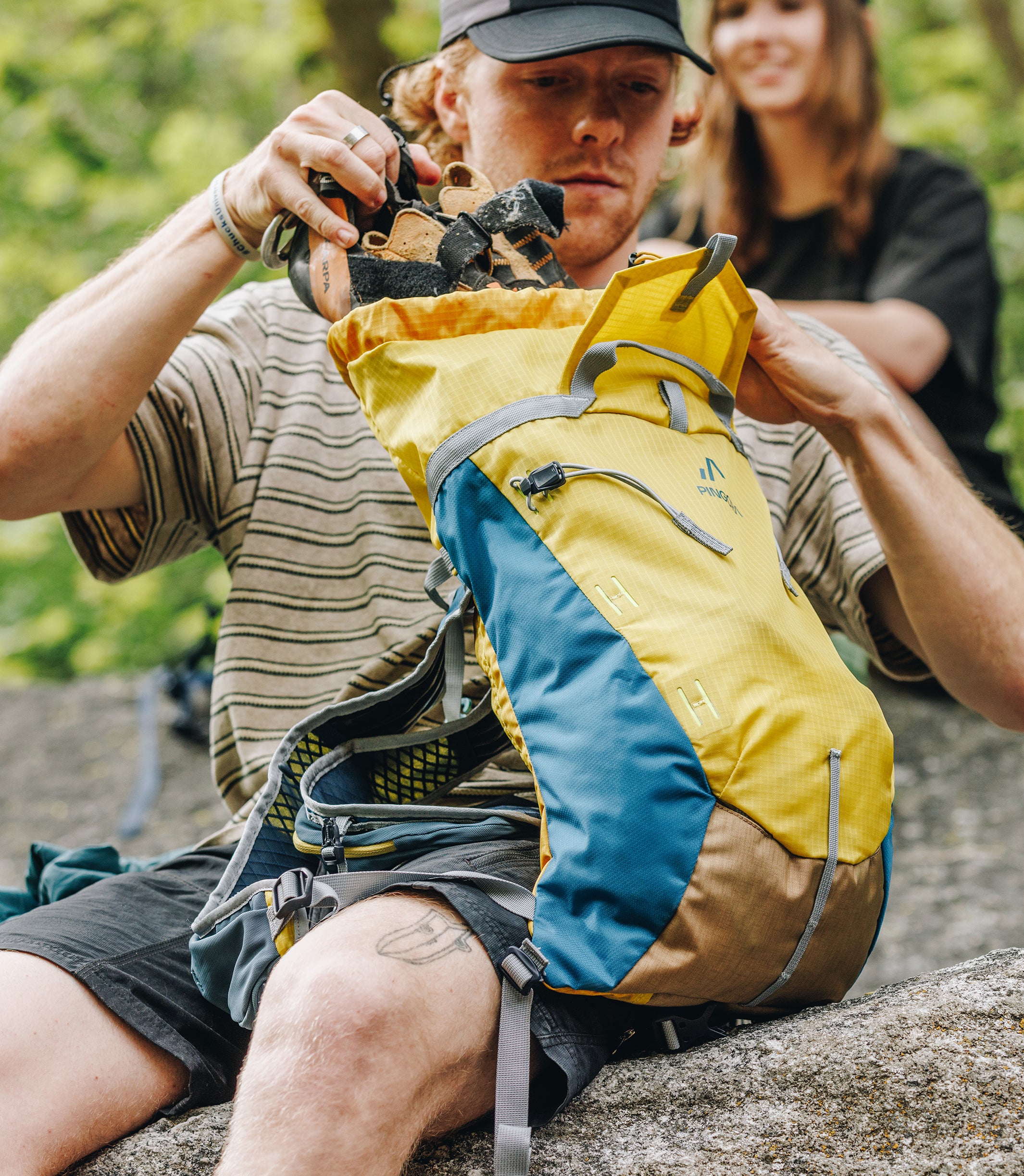 A live person using the Pingora Focus 15 liter climbing and hiking backpack in yellow and blue