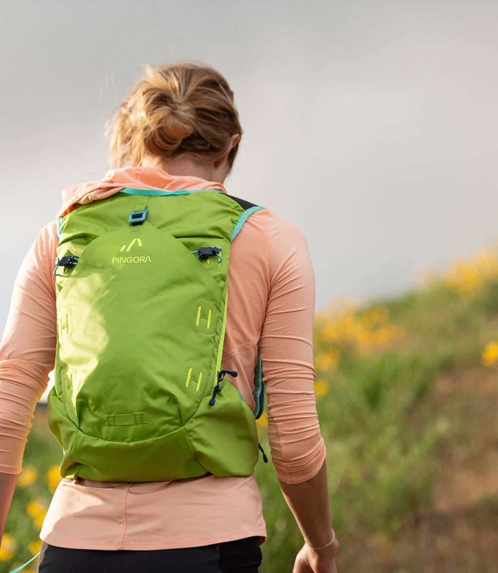 A green Pingora Impulse hydration pack designed for outdoor activities such as hiking and trail running, featuring multiple storage compartments and adjustable straps. Shown on models.