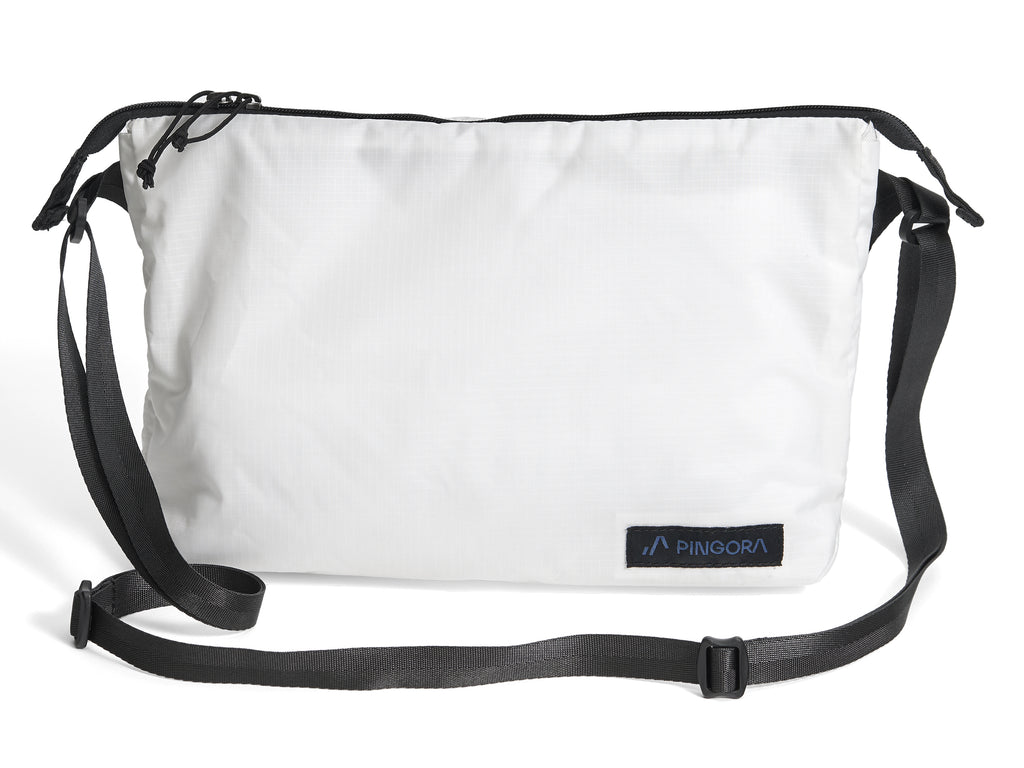 Pingora Satchel in white with black straps and a small blue logo on the front, designed for carrying items while backpacking or traveling.
